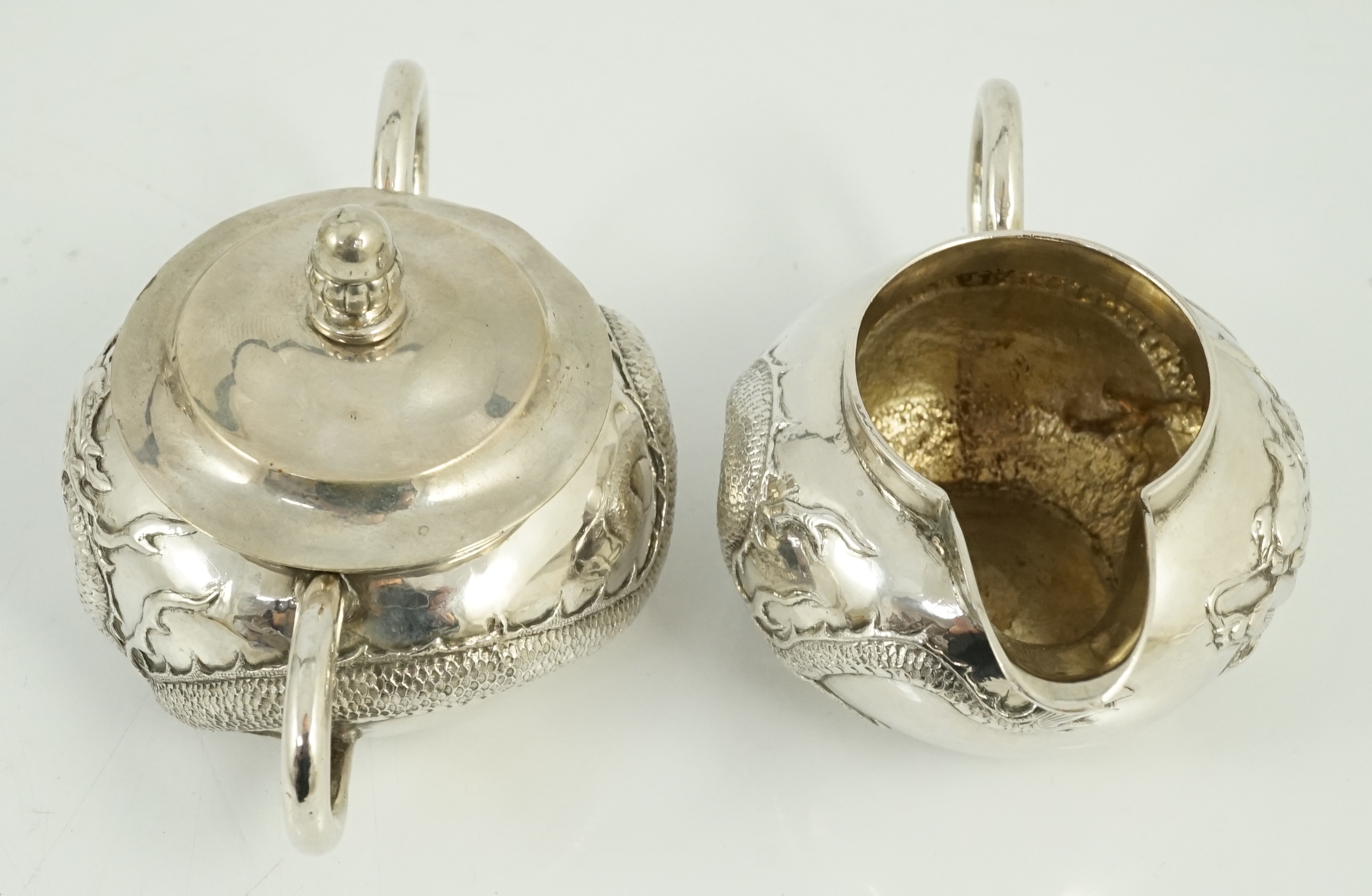 A Chinese three piece silver bachelor's tea set, by TC, decorated with dragon and one other similar Chinese silver two handled sugar bowl and cover, maker Sing Fat? and an odd cover